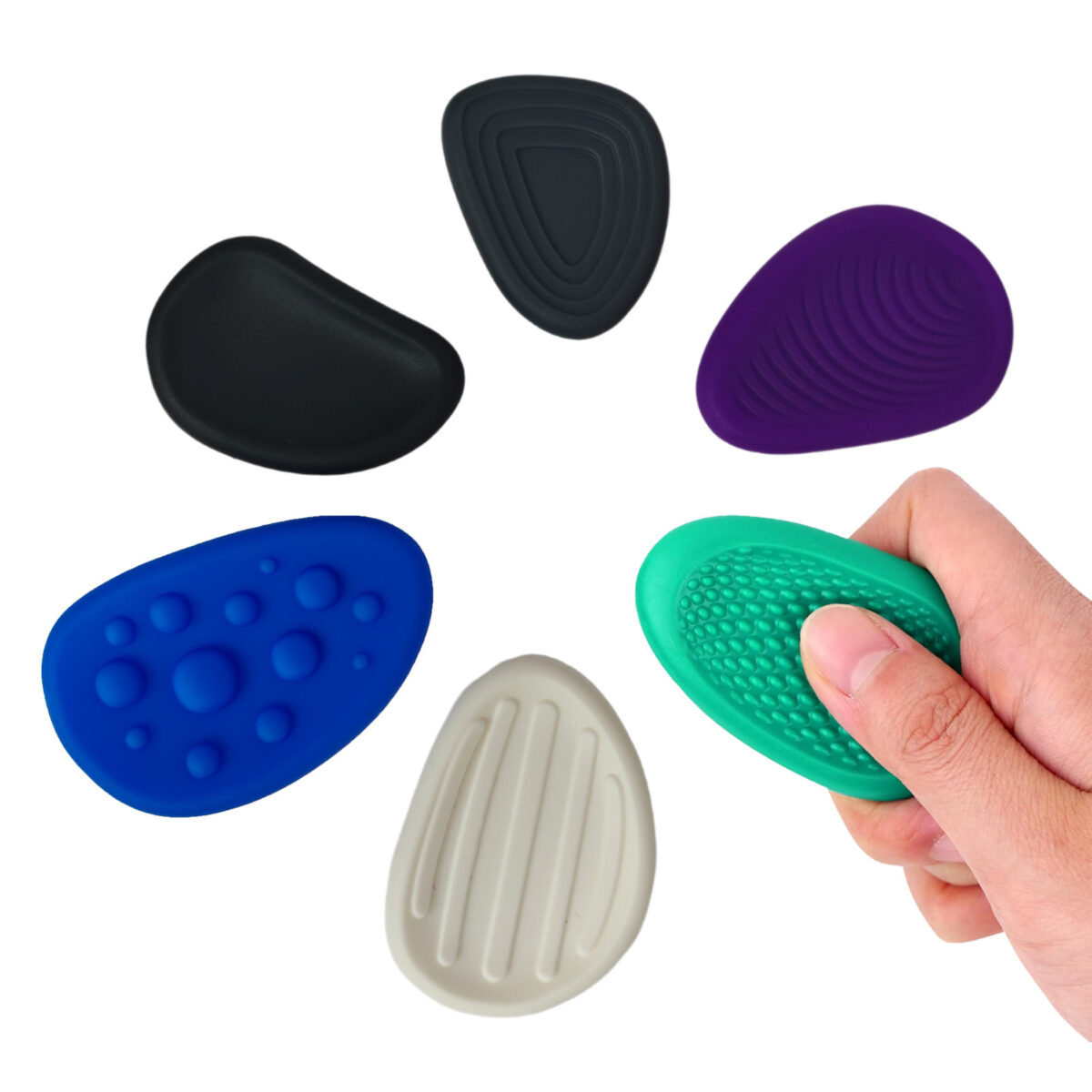 Les six galets sensoriels disposés en cercle, noir lisse, blanc à rainures, violet à nervures, vert à résille, anthracite à cercles et bleu à pastilles, avec une main qui en tient un