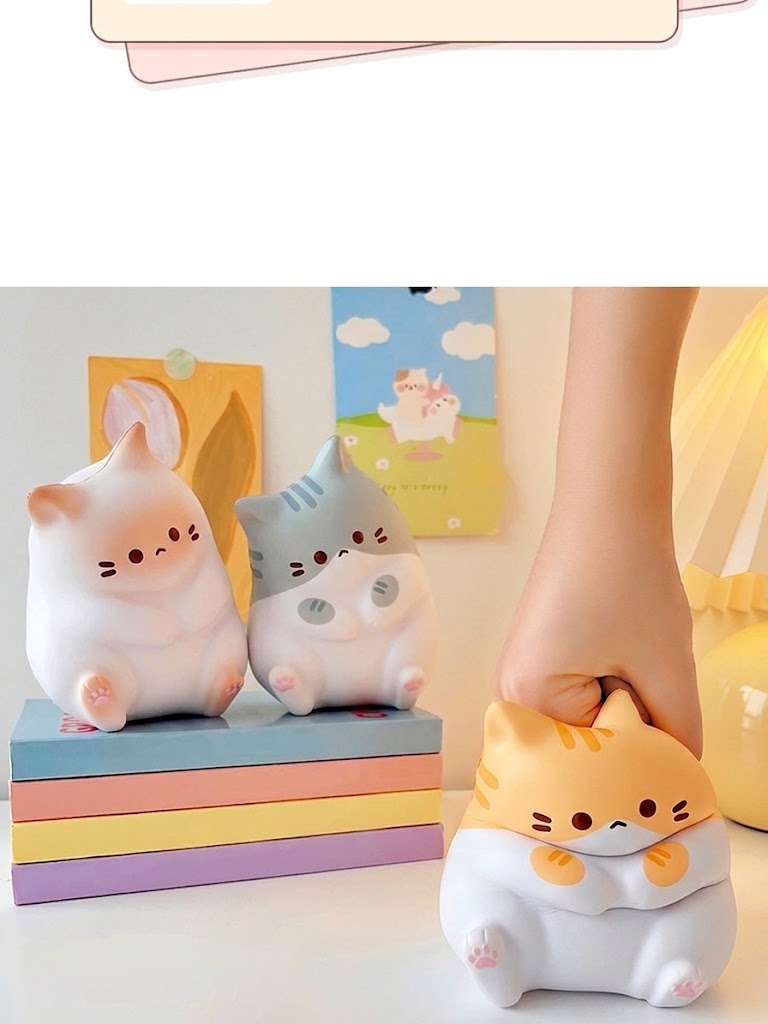 Deux veilleuses en forme de chats, blanche et grise, posées sur des livres aux couleurs pastel, une main pressant la version orange à droite